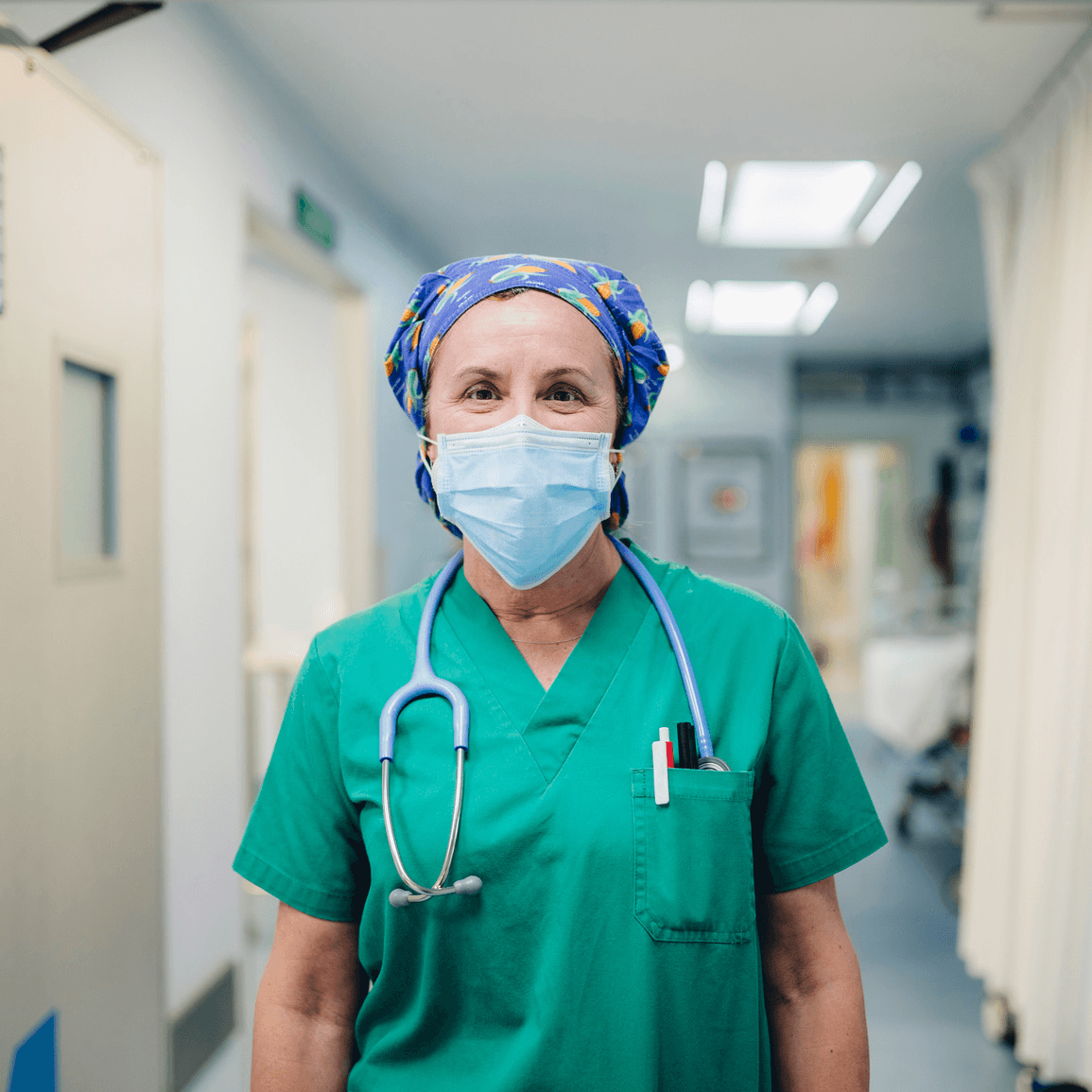 Pflegekraft in Kasack und Maske auf einem Krankenhausflur