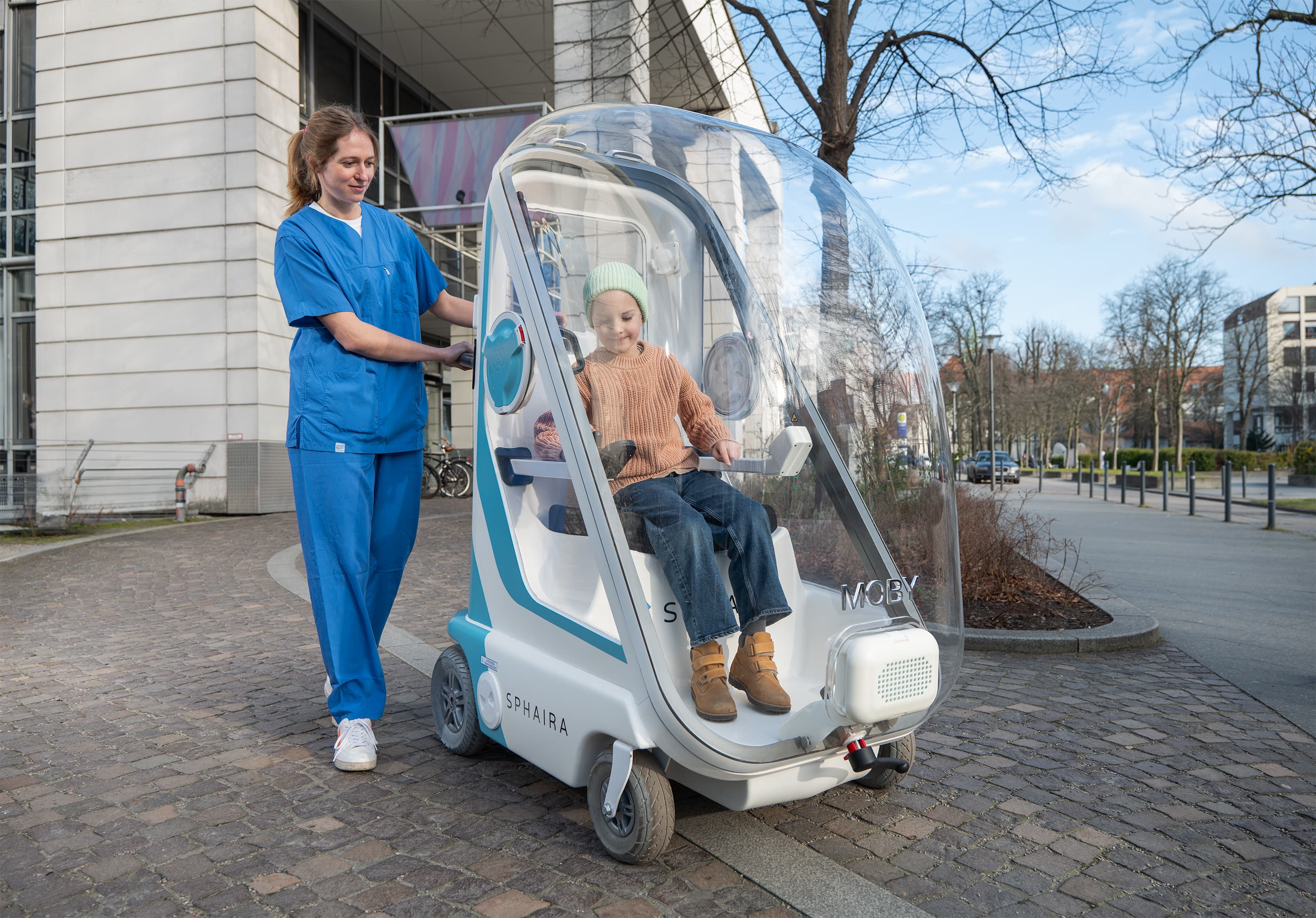 Pflegekraft schiebt ein Kind in einer MOBY-Kapsel vor einem Krankenhaus